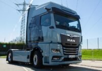 Front three-quarter view of a blue MAN electric semi-truck parked in a sunny lot, with '100% ELECTRIC' on the cab roof.