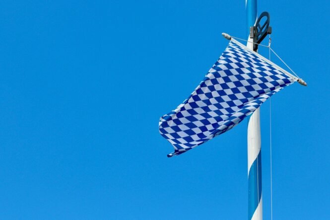Blue-and-white checkered Bavarian flag fluttering from a mast against a clear blue sky