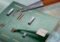 Close-up of a green printed circuit board with multiple small chips and gold contacts, as tweezers lift a connector from the board.