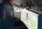 Researcher in a white lab coat loading sample tubes into a brightly lit laboratory analyzer.