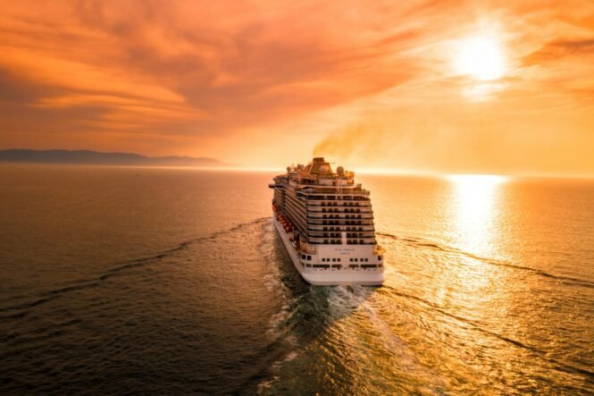 Cruise ship Royal Princess sailing at sunset with orange sky and calm ocean reflection.