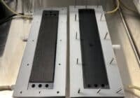 Two rectangular metal blocks with black textured inserts mounted on a metal base, each edged with metal pins around the perimeter.