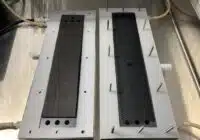 Two rectangular metal blocks with black textured inserts mounted on a metal base, each edged with metal pins around the perimeter.