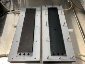 Two rectangular metal blocks with black textured inserts mounted on a metal base, each edged with metal pins around the perimeter.