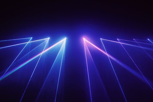 Laser light beams crisscross in blue and pink against a dark background, resembling a laser light show.