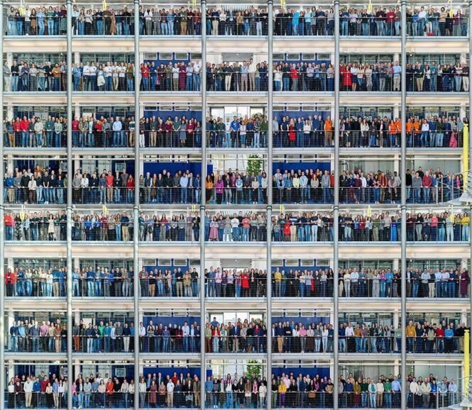 Large crowd of people on all floors of a multi-story office building, posing for a group photo.