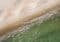Aerial view of a sandy beach meeting clear green water with gentle waves and sunlight glints.