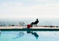 Person sitting in a chair at a rooftop pool, gazing over a distant cityscape.