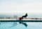 Person sitting in a chair at a rooftop pool, gazing over a distant cityscape.