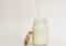 Milk is being poured into a glass mason jar with a metal lid resting on its side on a pale background.