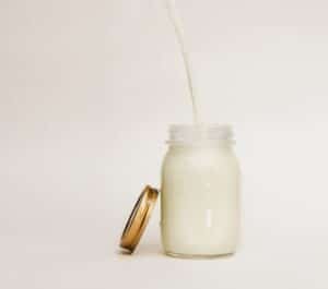 Milk being poured into a glass mason jar on a white background, with the lid resting beside it.