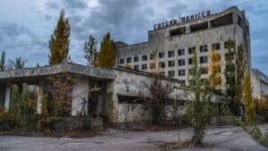 Abandoned hotel with cracked concrete facade, overgrown trees, and a statue near the entrance.