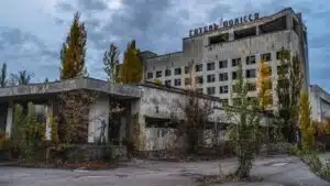 Abandoned hotel with cracked concrete facade, overgrown trees, and a statue near the entrance.