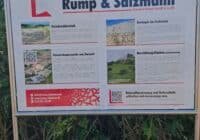 Outdoor information sign for Rump & Salzmann (Gipswerk Uehrde GmbH & Co. KG) with sections on stone quarrying and geology, images and descriptive text in German, mounted in a metal frame beside the path.