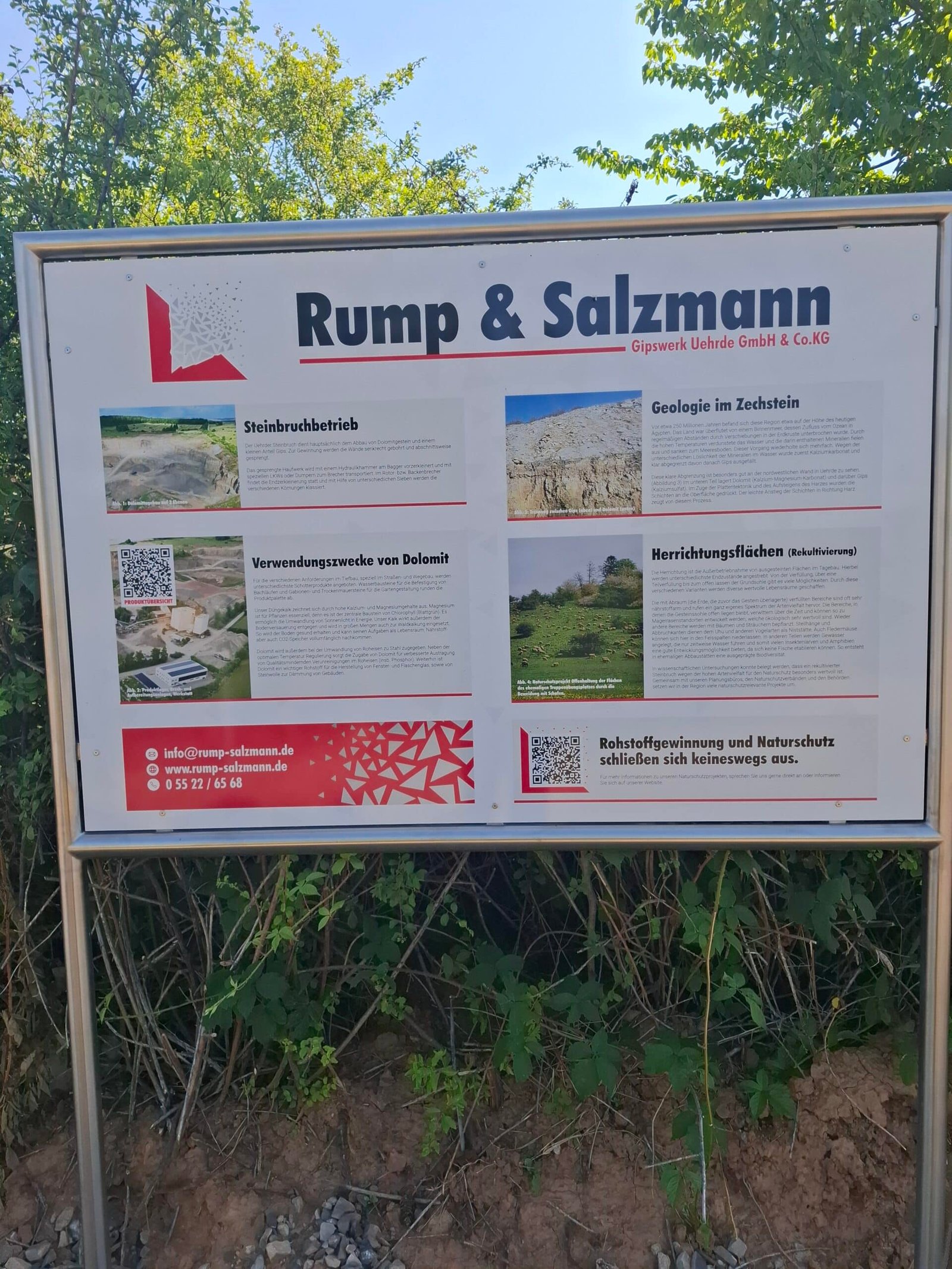 Outdoor information sign for Rump & Salzmann (Gipswerk Uehrde GmbH & Co. KG) with sections on stone quarrying and geology, images and descriptive text in German, mounted in a metal frame beside the path.