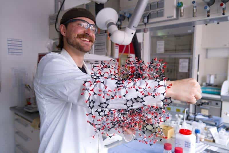 Erstautor Kalle Mertin demonstriert die poröse Struktur von CAU-10-H anhand eines Modells: Dass sein Arm hindurchpasst, veranschaulicht die durchgehenden, röhrenartigen Poren, in denen das Material Wassermoleküle aufnimmt und wieder freisetzt. | Copyright: Christina Anders, Uni Kiel
