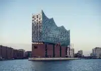 Elbphilharmonie concert hall with a wavy glass facade rising from a brick base by Hamburg harbor, reflected in the water.5c2 The iconic Hamburg building with a glassy, curved roof on the riverfront.5c2