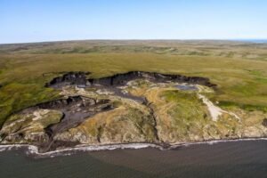Aerial view of rugged shoreline with eroded cliffs, green plains, and tidal pools along the coast.