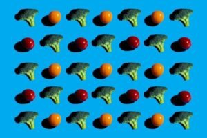 Repeating grid of broccoli florets and small orange and red tomatoes on bright blue background.