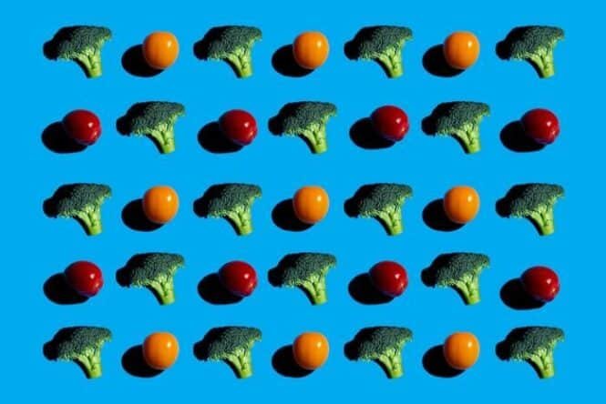 Repeating grid of broccoli florets and small orange and red tomatoes on bright blue background.