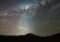 Silhouette of a person on a hill at night, with a bright light casting rays across a star-filled sky and streaking meteor trails.