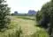 Open rural landscape with a dirt path through a field, flanked by trees on both sides and distant rocky cliffs on the horizon.