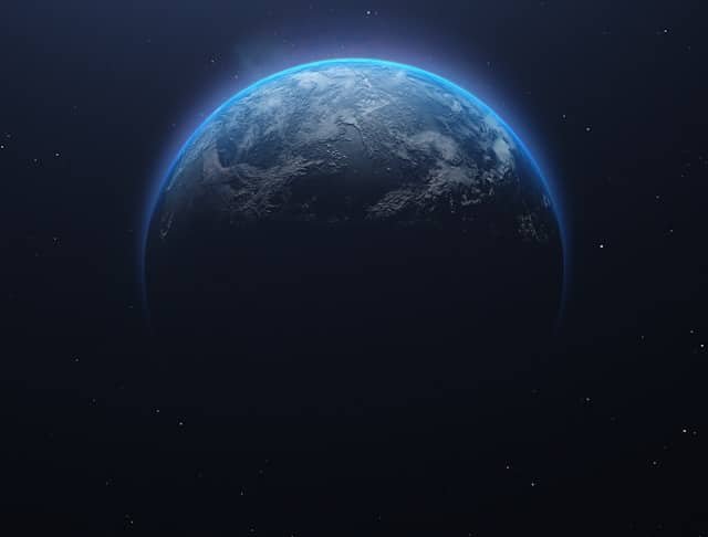 Partial view of Earth from space with a blue glow along the limb and stars in the background, mostly dark.