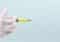 Gloved hand holding a syringe filled with yellow liquid and a long needle against a pale background. The image implies a medical injection is prepared.