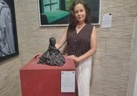 Woman in a brown sleeveless blouse posing with a dark abstract sculpture on a red pedestal in a gallery.