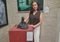 Woman in a brown sleeveless blouse posing with a dark abstract sculpture on a red pedestal in a gallery.