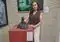 Woman in a brown sleeveless blouse posing with a dark abstract sculpture on a red pedestal in a gallery.