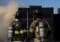 Two firefighters in full turnout gear with SCBA tanks stand side by side, facing a smoky black structure at a training or incident scene.