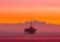 Offshore oil rig standing on stilts in the calm sea at sunset with a vivid orange and pink sky.