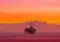 Offshore oil rig standing on stilts in the calm sea at sunset with a vivid orange and pink sky.