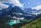 Turquoise alpine lake nestled among evergreen forests and snow-capped mountains under a blue sky.