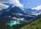Turquoise alpine lake nestled among evergreen forests and snow-capped mountains under a blue sky.
