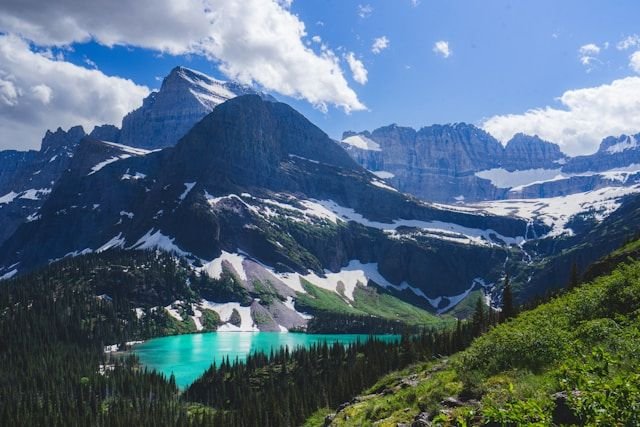 Turquoise alpine lake nestled among evergreen forests and snow-capped mountains under a blue sky.
