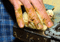 Adult hand gently restraining a fluffy yellow chick on a metal surface, showing the tiny bird’s beak and feet clearly.