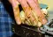Adult hand gently restraining a fluffy yellow chick on a metal surface, showing the tiny bird’s beak and feet clearly.