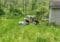 Group of people crouching in tall grass near a small shed, collecting samples or doing fieldwork with coolers and bags nearby.