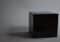 A matte black cube sits on a gray surface with a soft shadow to its left in a neutral studio setting.