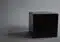 A matte black cube sits on a gray surface with a soft shadow to its left in a neutral studio setting.