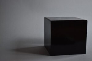 Black cube on a gray surface, casting a soft shadow to the left.