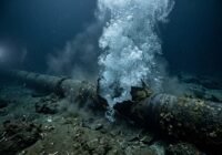Rusted subsea pipe bursting, sending a column of bubbles and steam up from the ocean floor.