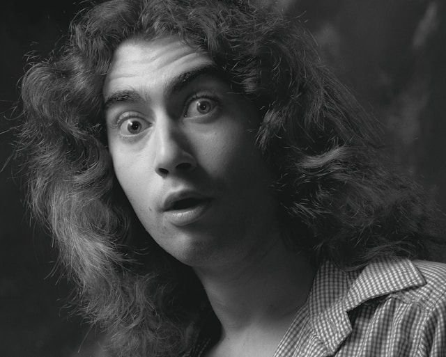 Black-and-white portrait of a woman with surprised expression, wide eyes, slightly open mouth, wearing a checkered shirt collar.