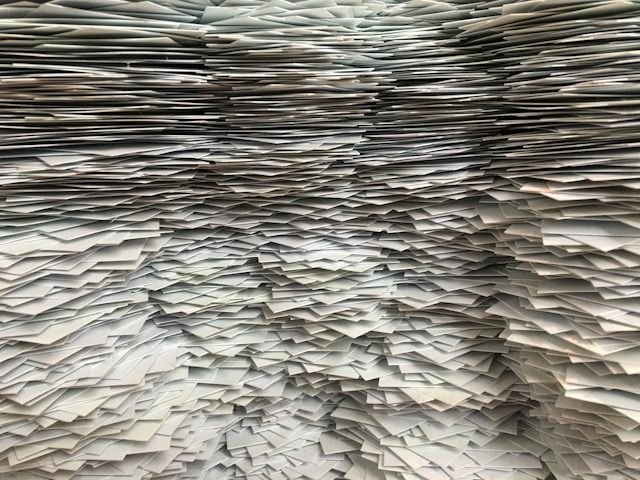 Wall of stacked papers forming a narrow, tunnel-like corridor of overlapping sheets.