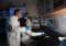 Three researchers in lab coats, two standing and one seated, analyze a computer monitor showing a blue?and?red graph.