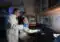 Three researchers in lab coats, two standing and one seated, analyze a computer monitor showing a blue?and?red graph.