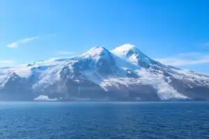 Snowy mountain range rising from a calm blue fjord under a clear sky