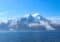 Snowy mountain range rising from a calm blue fjord under a clear sky
